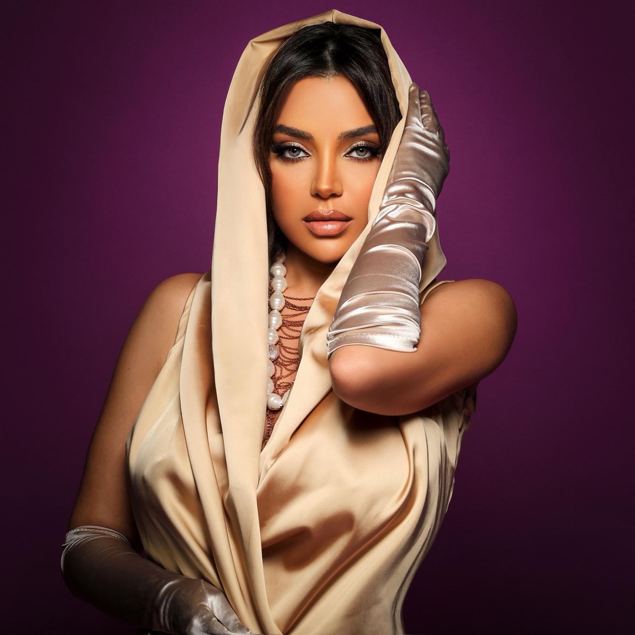 Jana Rouhana in a champagne-gold hooded gown with white gloves against a plum backdrop